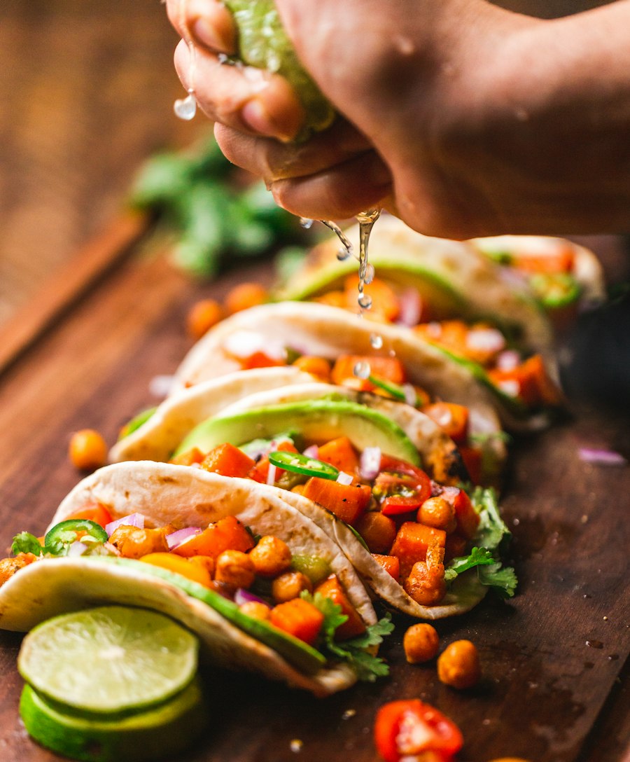 A hand squeezing lime over a row of loaded tacos